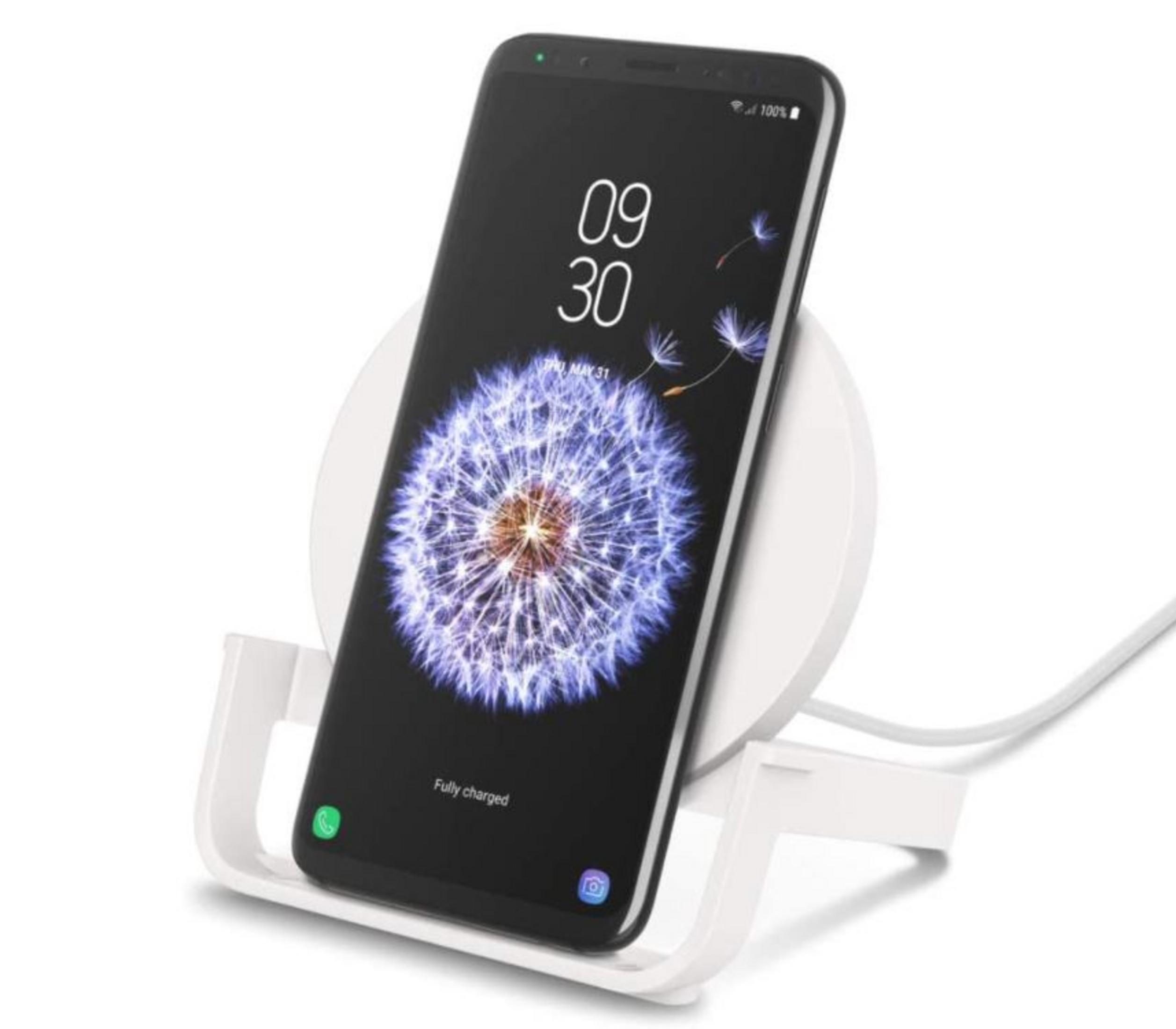Un smartphone con fondo de diente de león en un soporte de carga blanco.