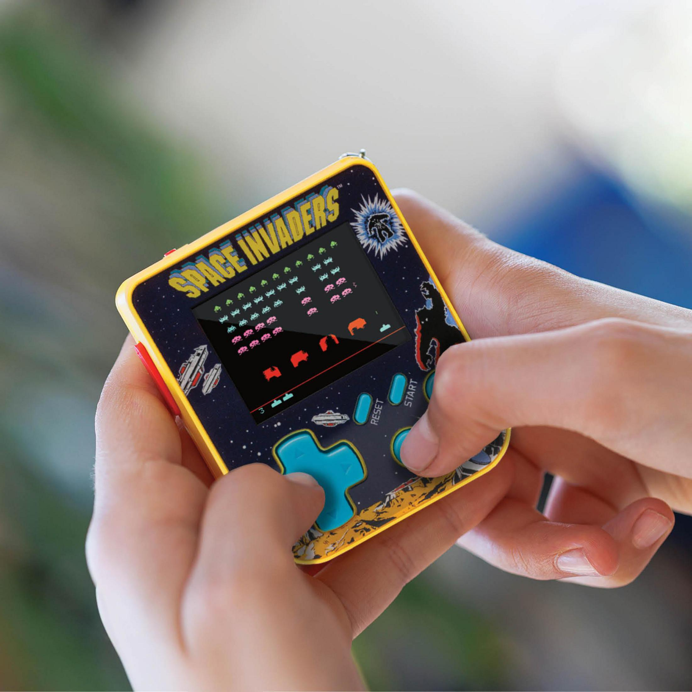 Manos sosteniendo un juego portátil amarillo de Space Invaders con cruceta azul.