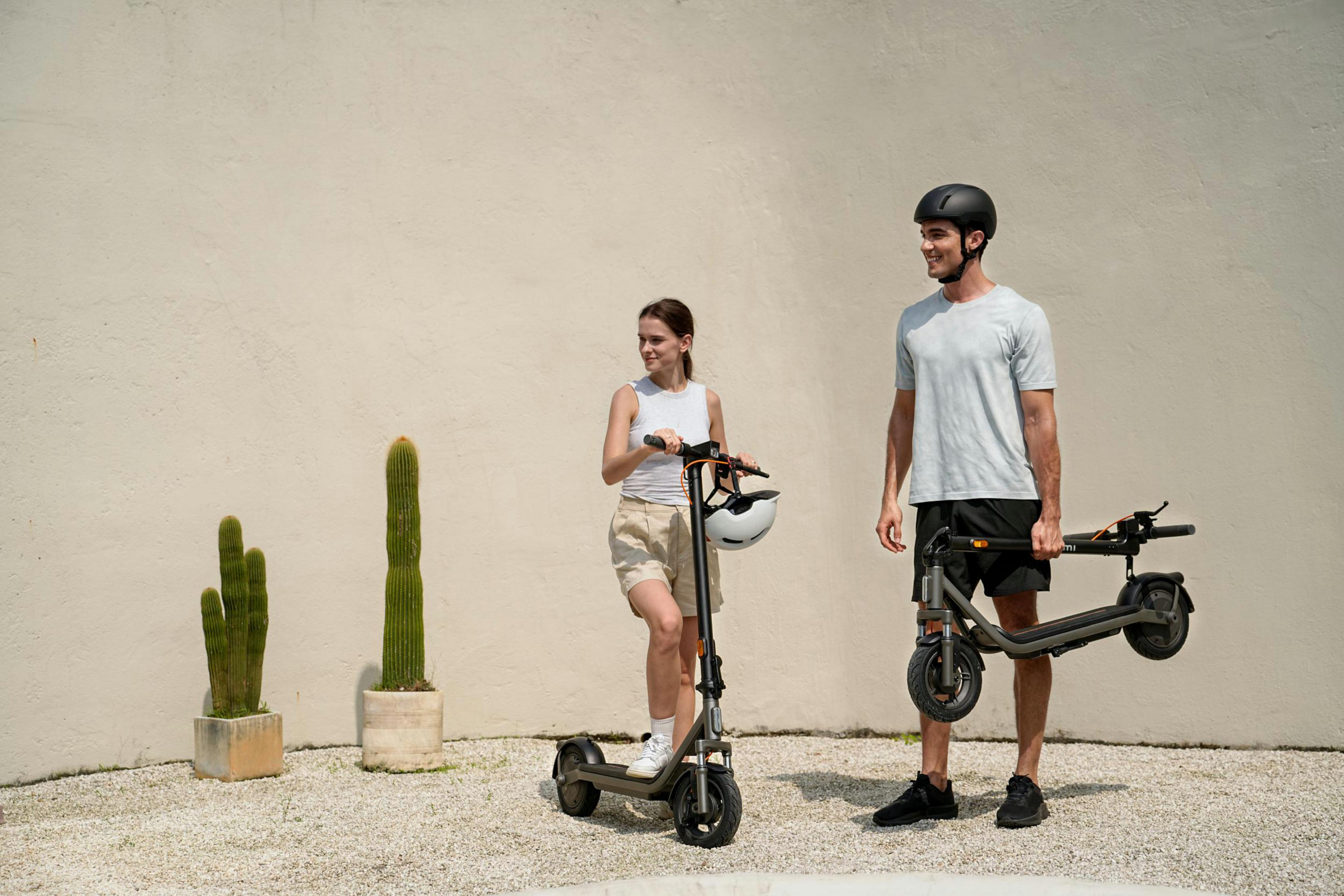 Uomo e donna con e-scooter davanti a un muro con cactus.