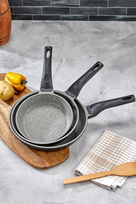 Patates ve biberli ahşap tahta üzerinde farklı boyutlarda üç tava.