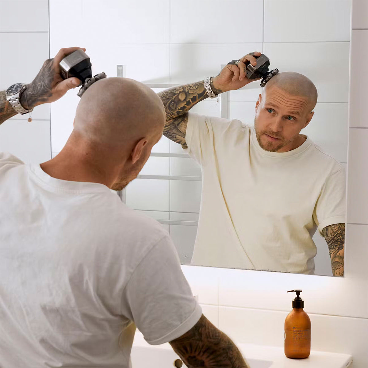 Hombre se afeita la cabeza en el espejo del baño con una recortadora.