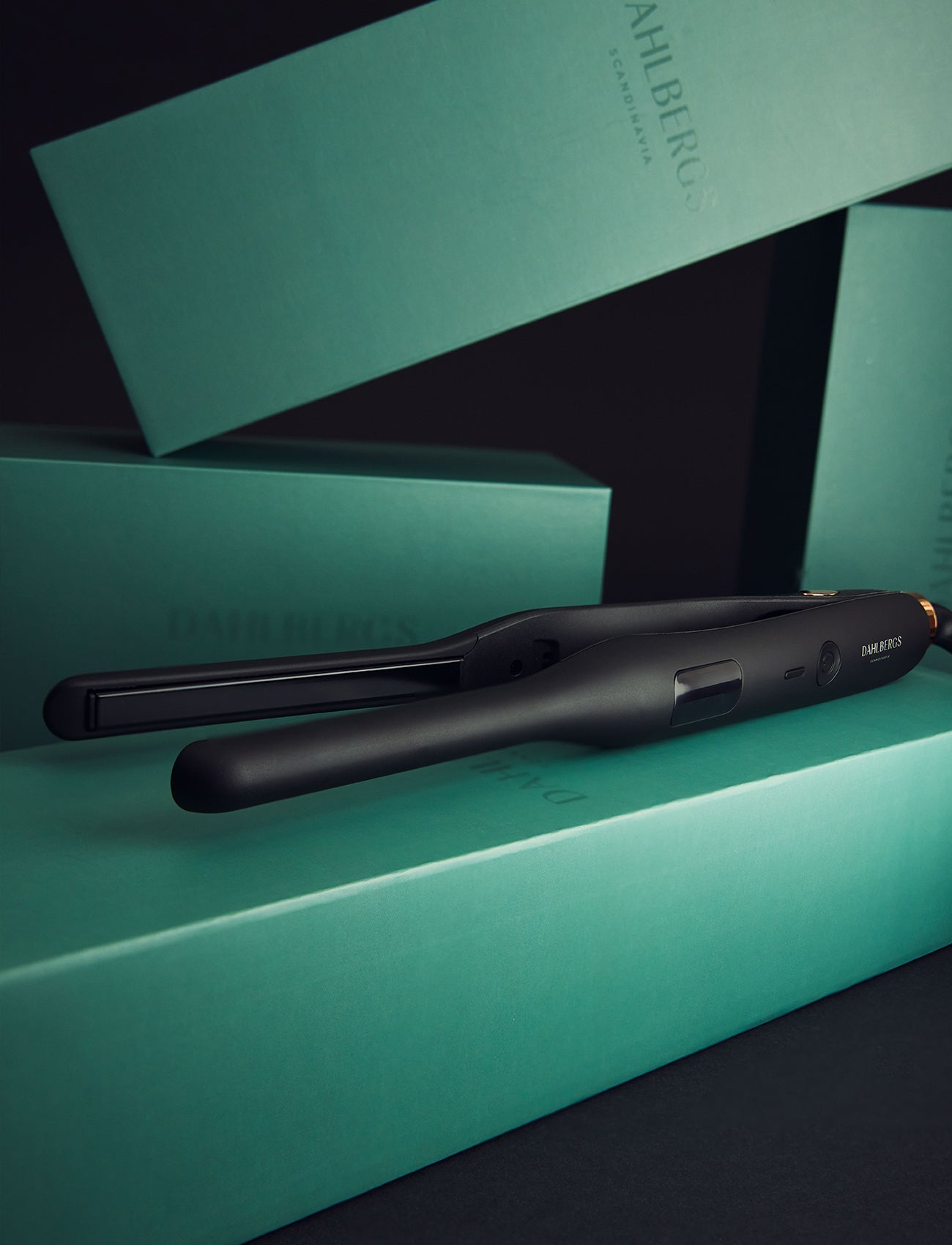 Una plancha de pelo negra descansa sobre una caja verde azulado con la marca DAHLBERGS.