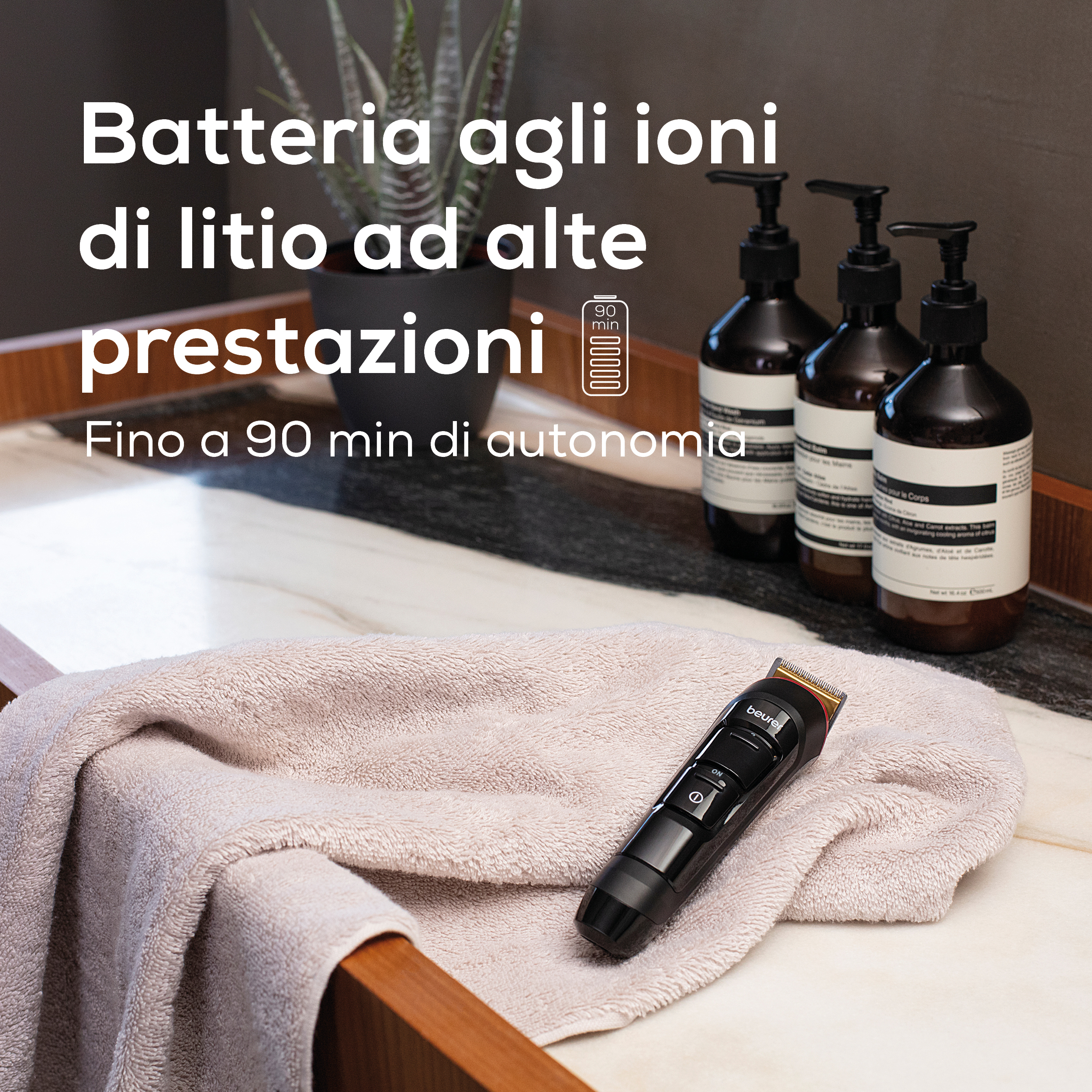 Un tagliacapelli nero riposa su un asciugamano beige chiaro. Tre dispenser di sapone scuri sono sullo sfondo.