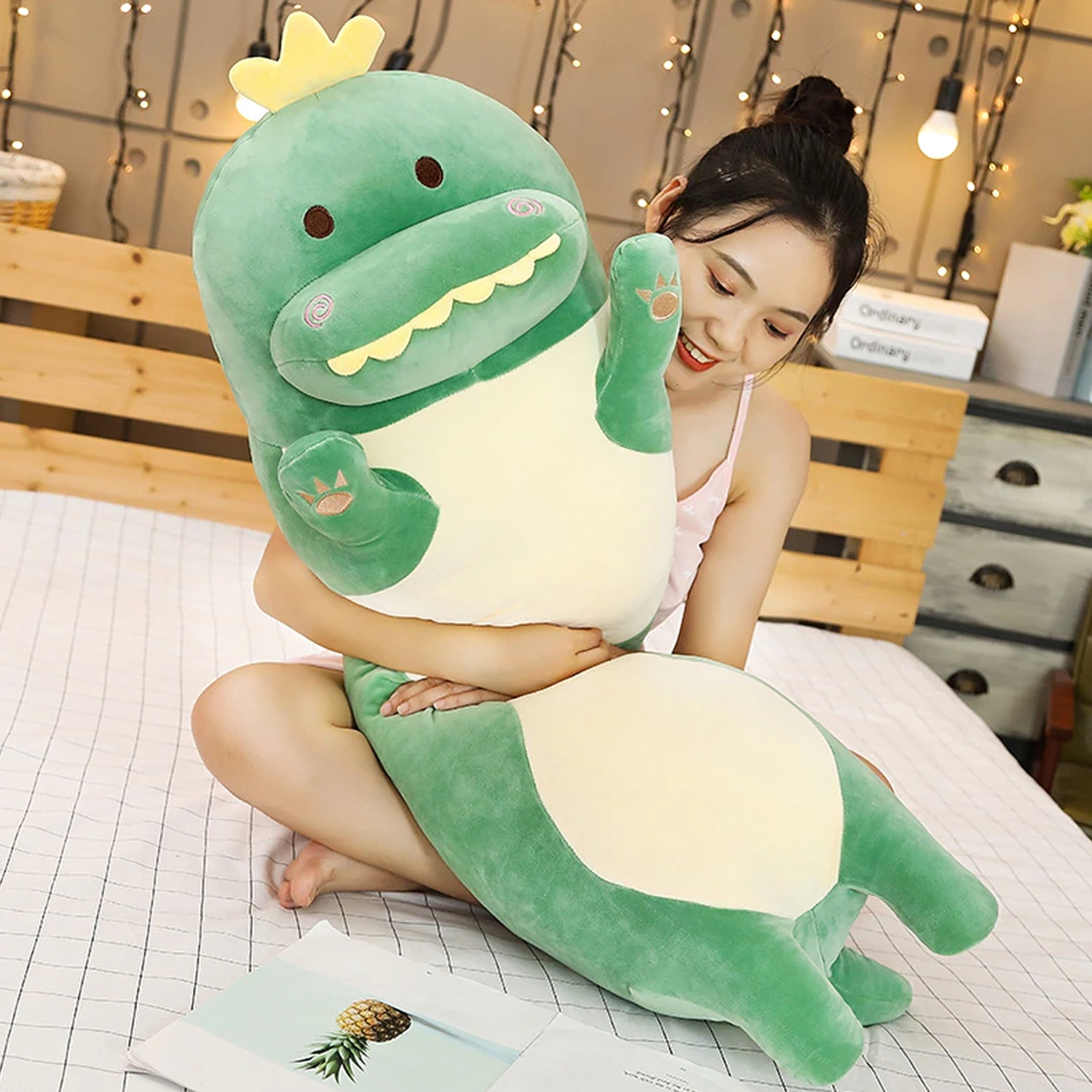 Una donna seduta su un letto tiene un grande dinosauro di peluche verde con una corona gialla.