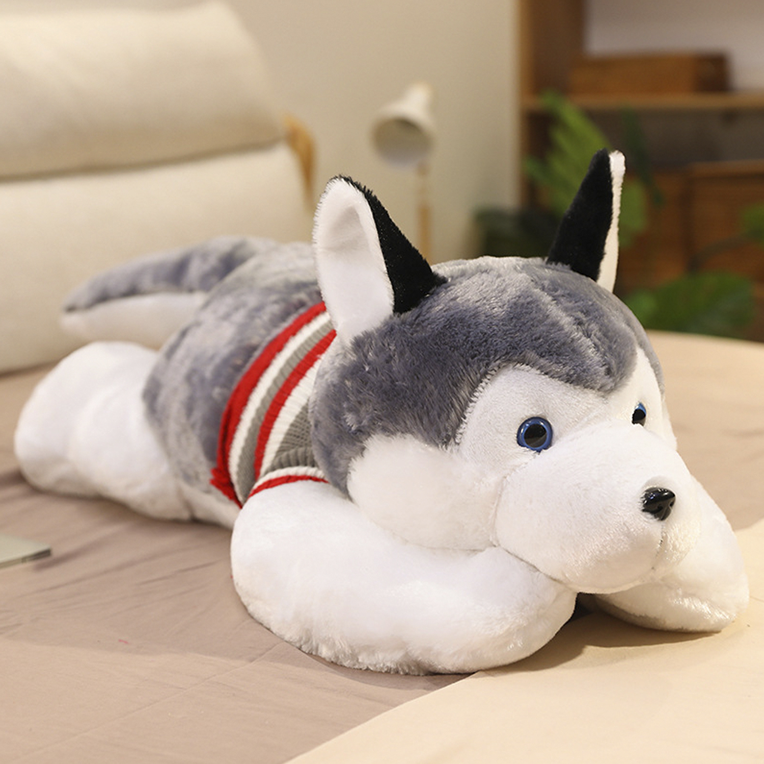 Un cane husky di peluche con maglione blu giace su un letto.