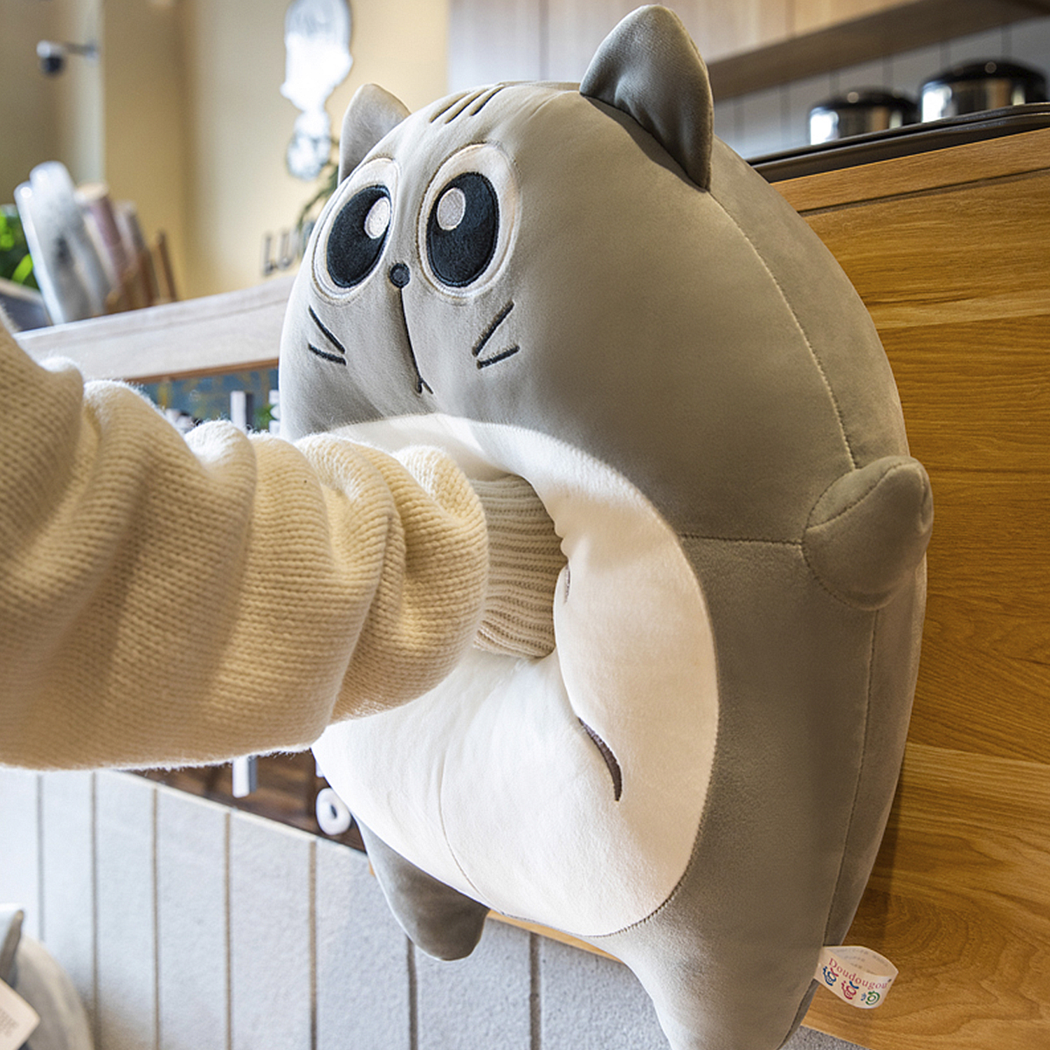Un peluche grigio a forma di gatto con occhi grandi, in cui una mano si inserisce.