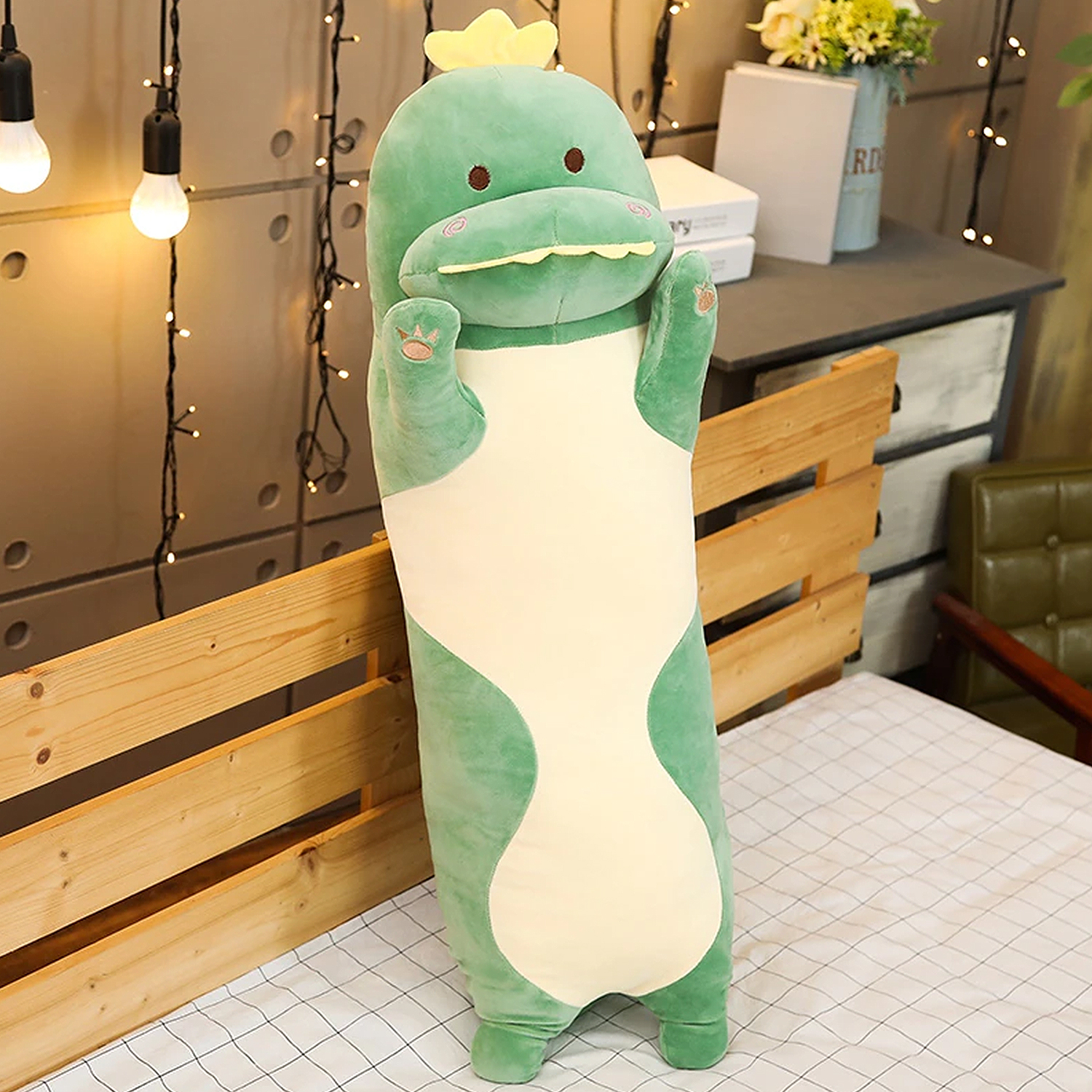 Un peluche di dinosauro verde con corona gialla sta su un letto.