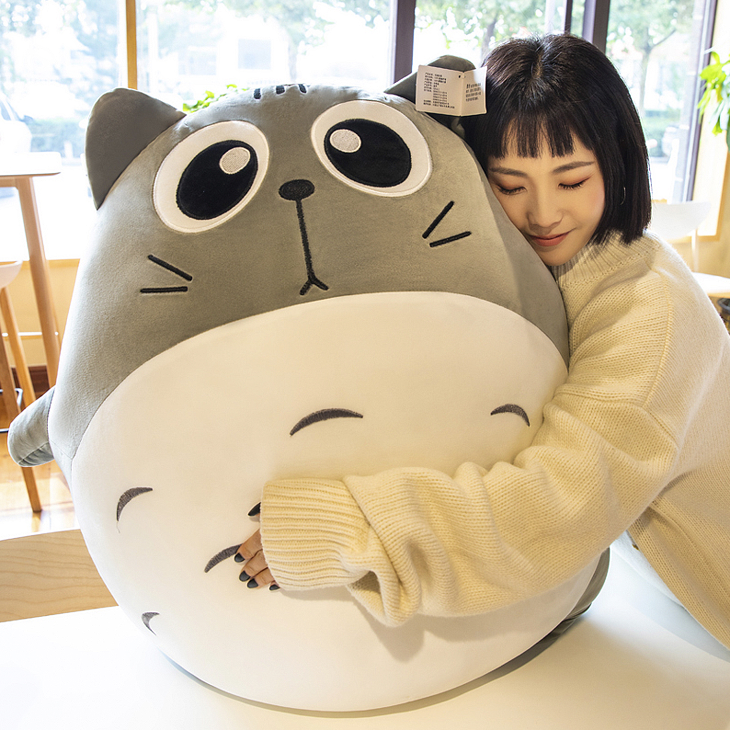 Una donna abbraccia un grande personaggio Totoro di peluche grigio.