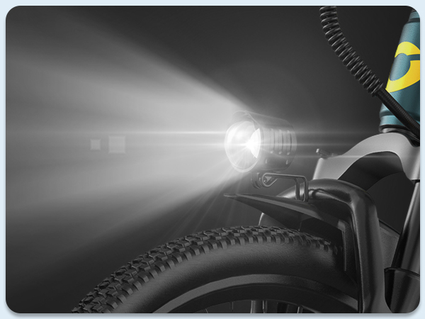 Primo piano di un faro di bicicletta illuminato, con parte della ruota e del manubrio visibili.