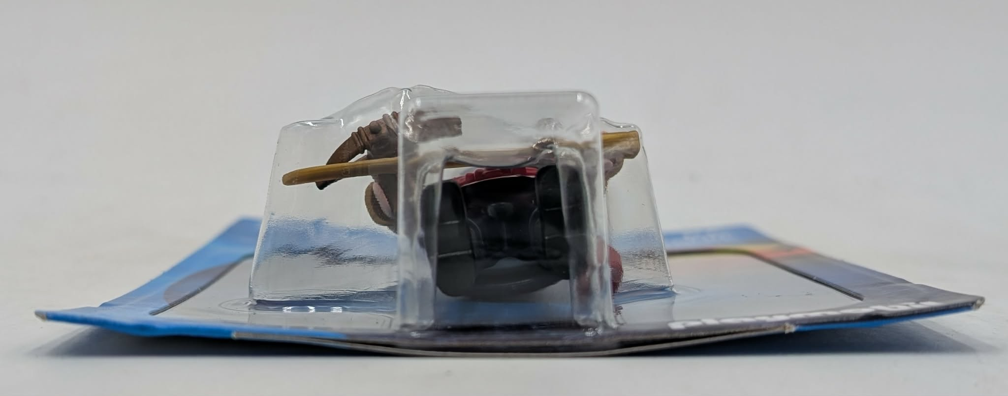 Un personaggio marrone e appuntito che tiene un bastone giallo in una confezione di plastica.