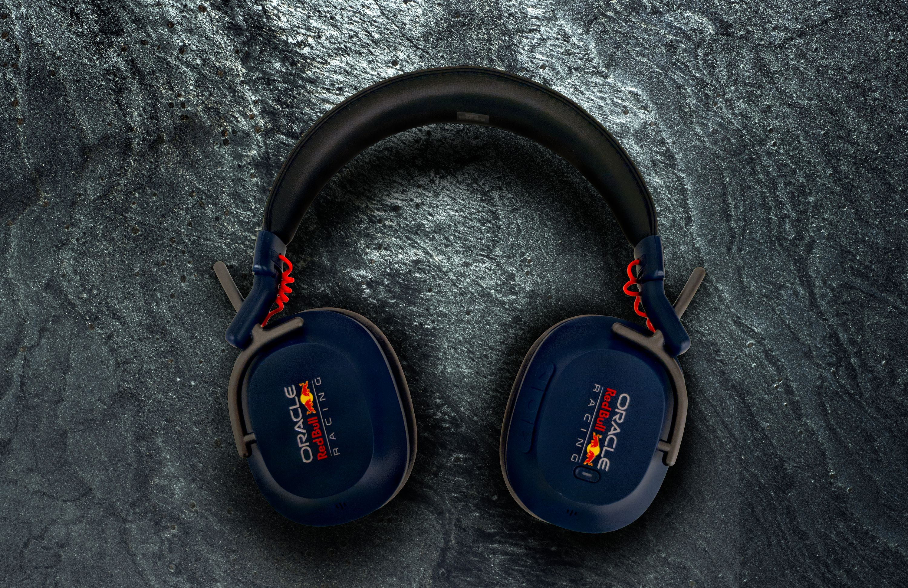 Dunkelblaue Kopfhörer mit Red Bull Racing-Logo auf dunklem Steinuntergrund.