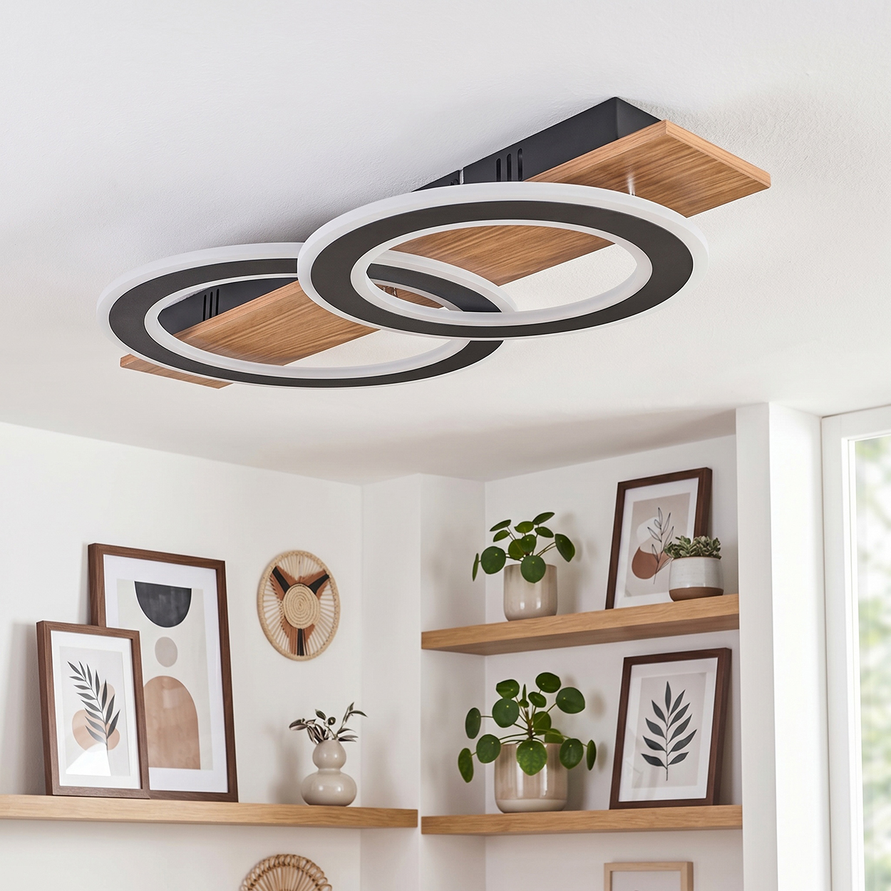 Eine moderne Deckenleuchte mit Holzdetails und zwei Ringen, über einem Regal mit Bildern und Pflanzen.