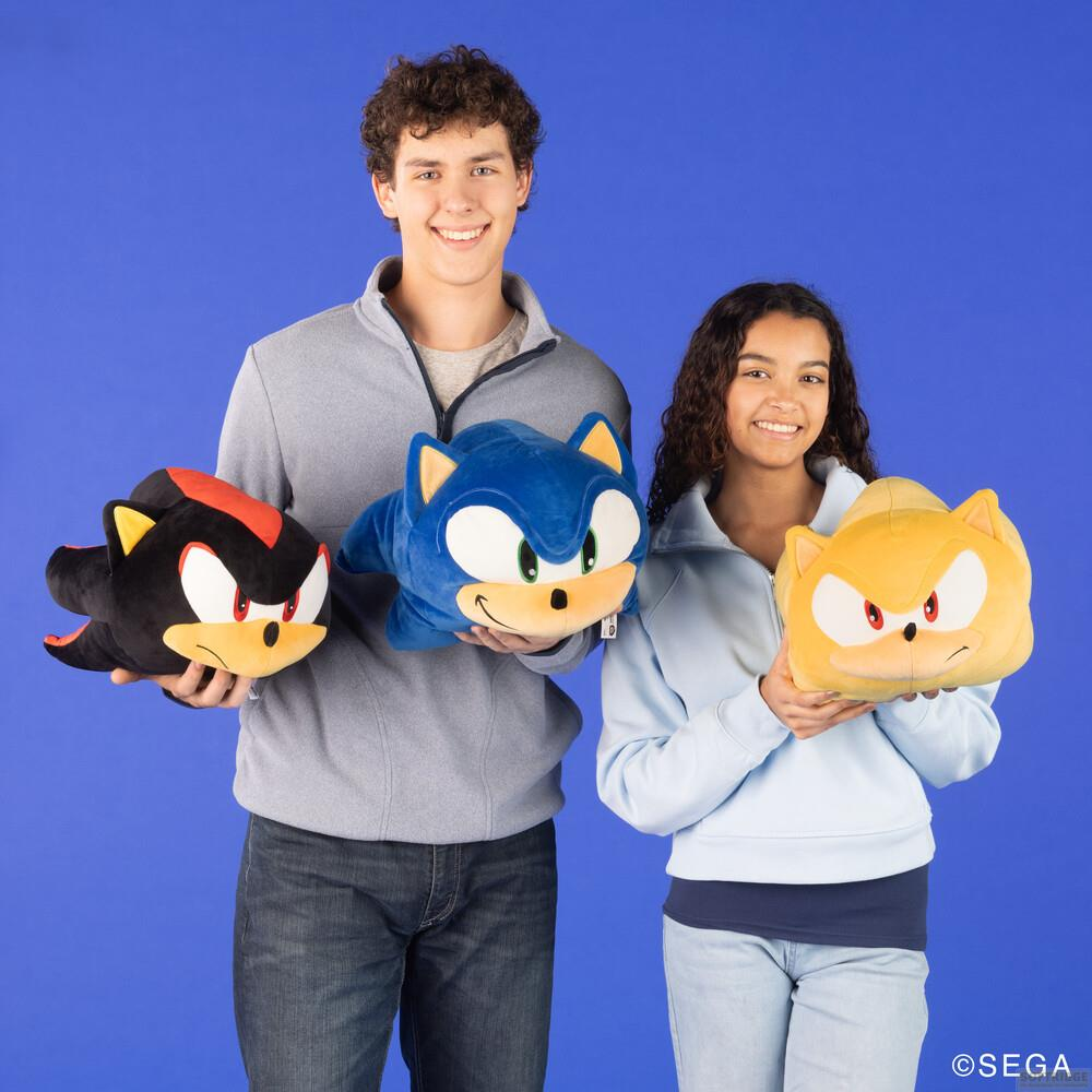 Due bambini tengono peluche: Sonic, Shadow e Tails su sfondo blu.