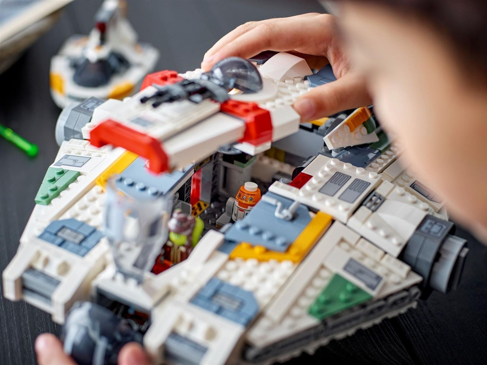 Kind baut ein weißes Raumschiff aus LEGO-Steinen mit roten und gelben Akzenten.