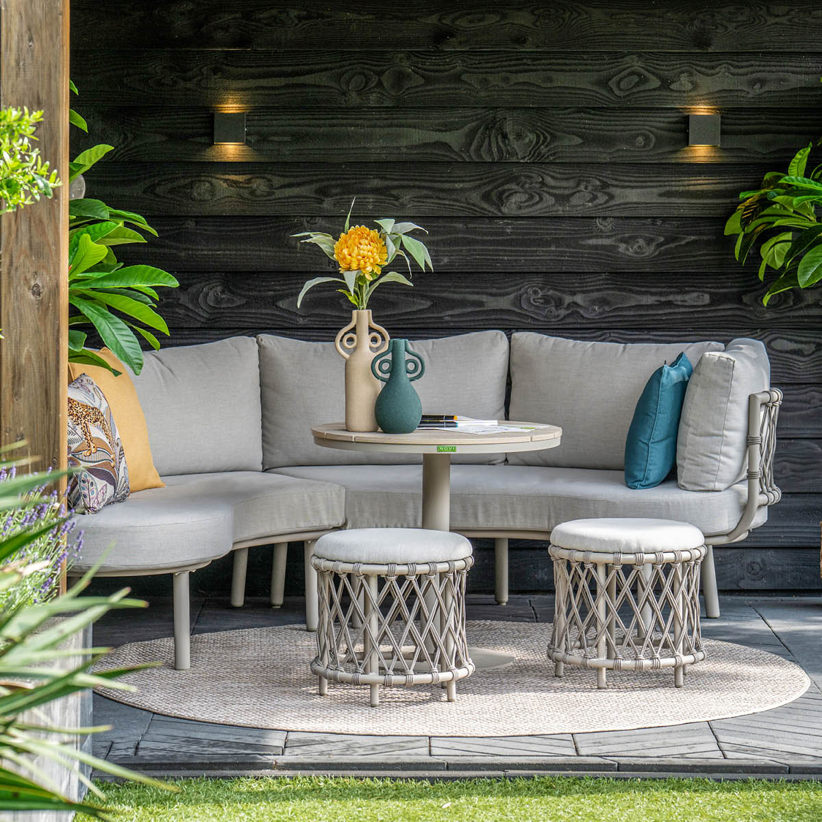 Buitenlounge met lichtgrijs bankstel, bijzettafel, twee krukjes en planten.