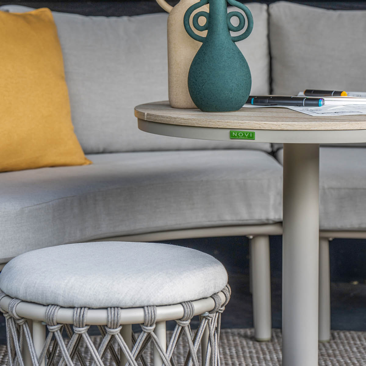 Een ronde tafel met twee vazen, stiften en een geel kussen op een bank.