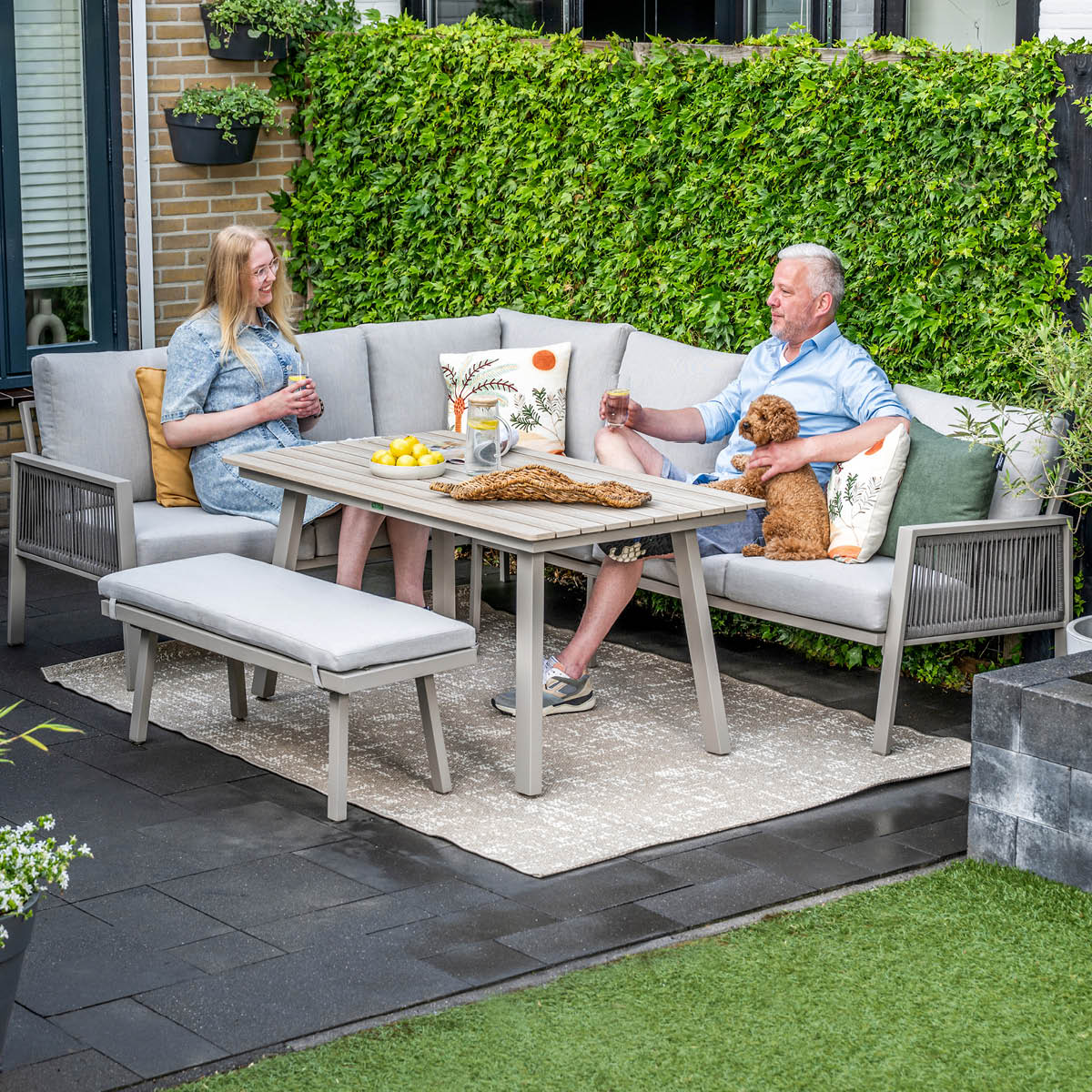 Koppel met hond ontspant op tuinstoel. Tafel met citroenen en drankjes.