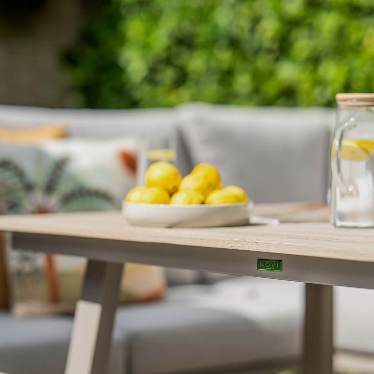 Een kom met citroenen en een glazen kan water op een tuintafel.