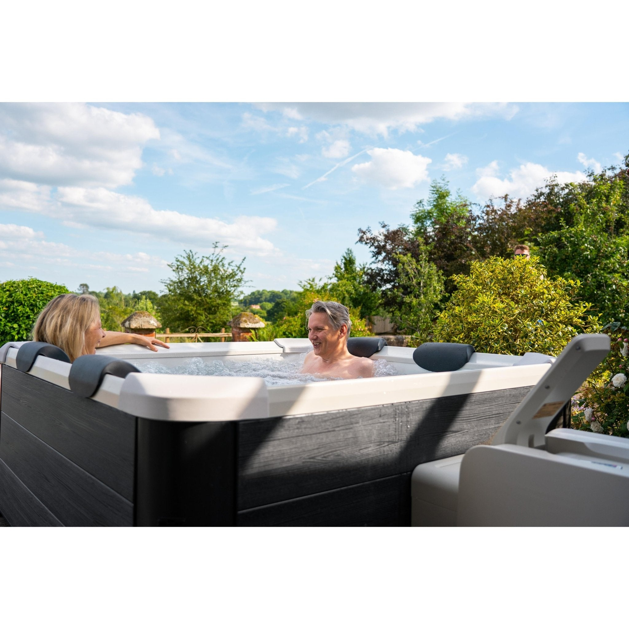 Un hombre y una mujer se relajan en un jacuzzi exterior rodeado de vegetación.