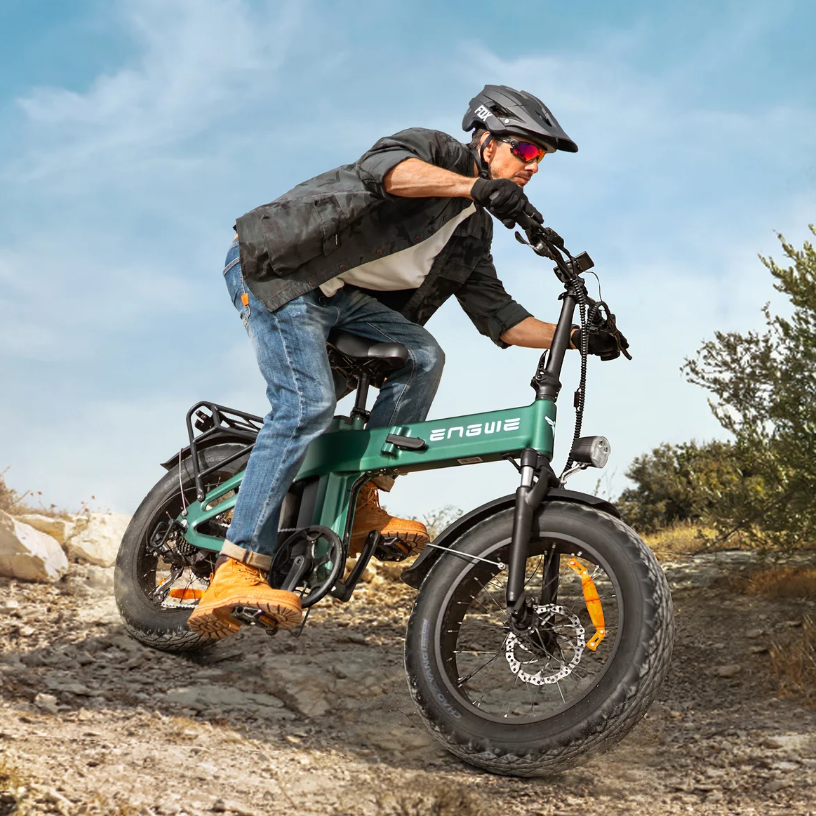 Mann fährt ein grünes E-Bike auf einem Feldweg mit Felsen und Büschen.