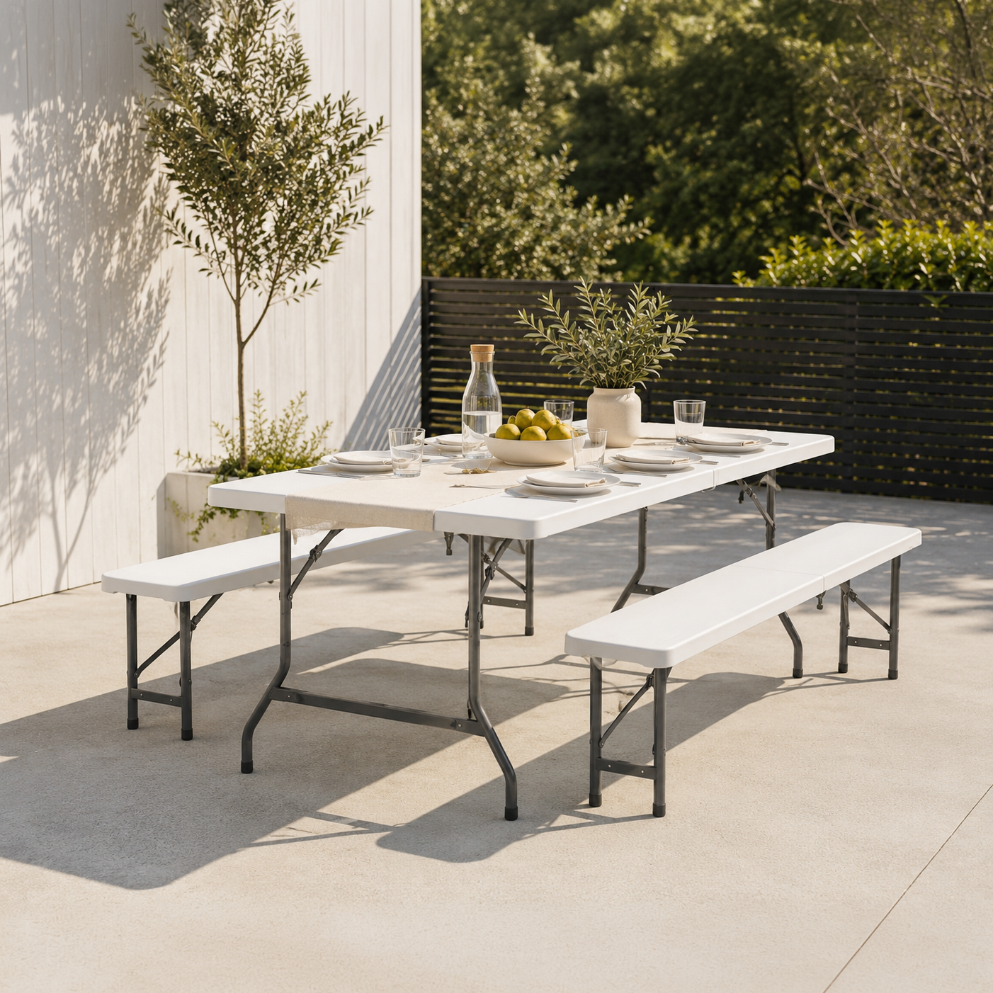 Una mesa blanca de exterior con bancos, puesta para una comida, con fruta y vasos.