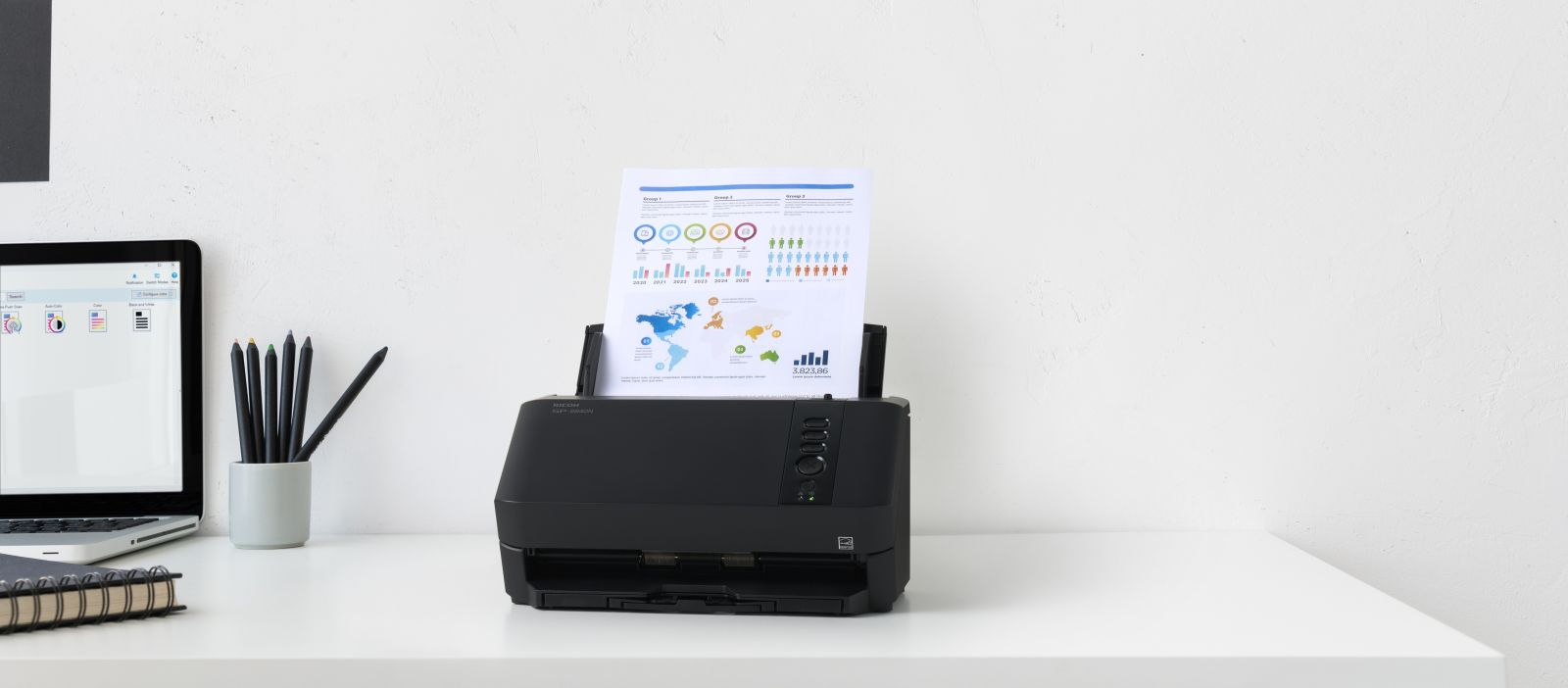 Ein schwarzer Drucker scannt ein Dokument mit Diagrammen und Karten. Ein Laptop und Stifte sind daneben.