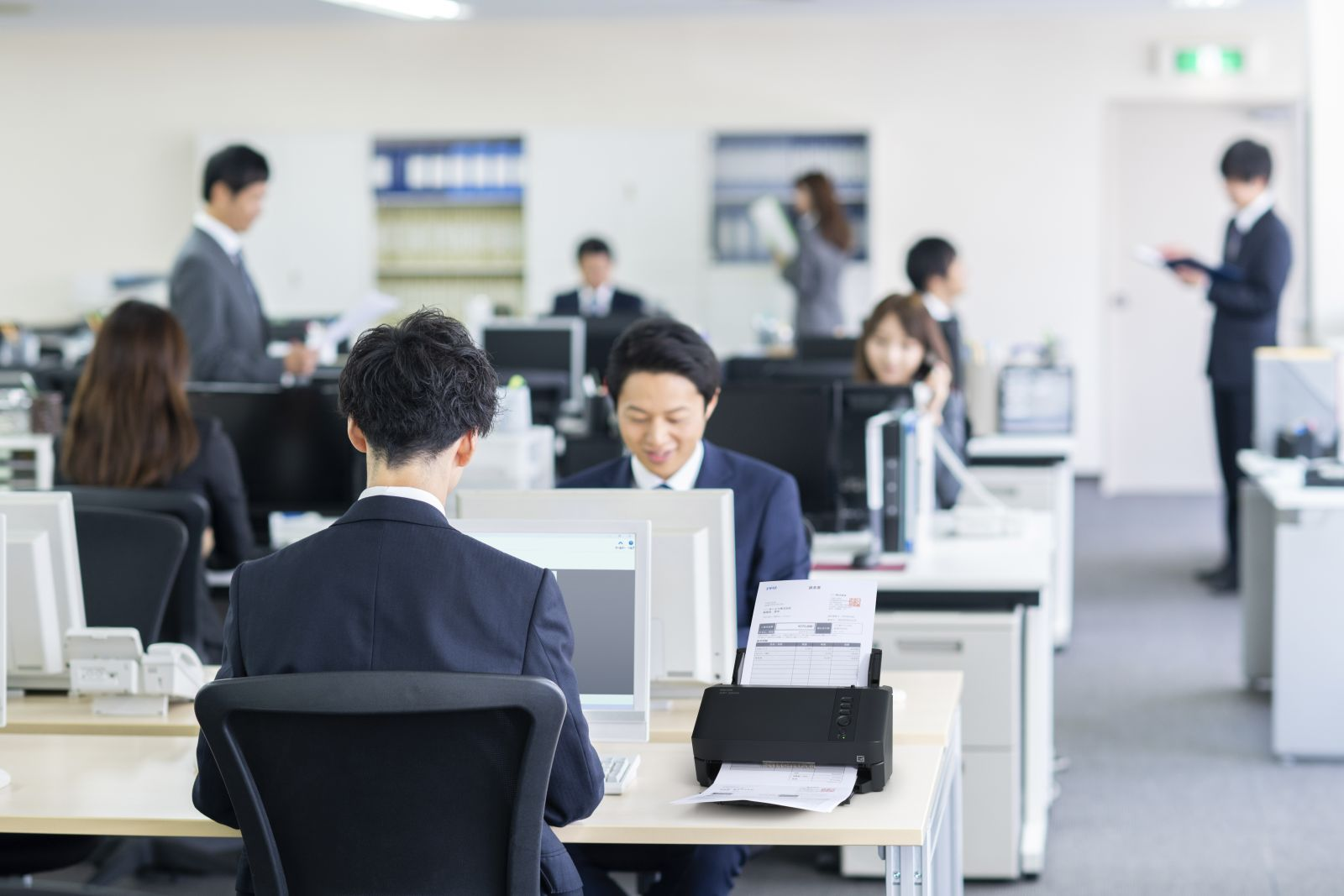 Büro mit Angestellten, die an Computern arbeiten, einer mit einem Scanner.
