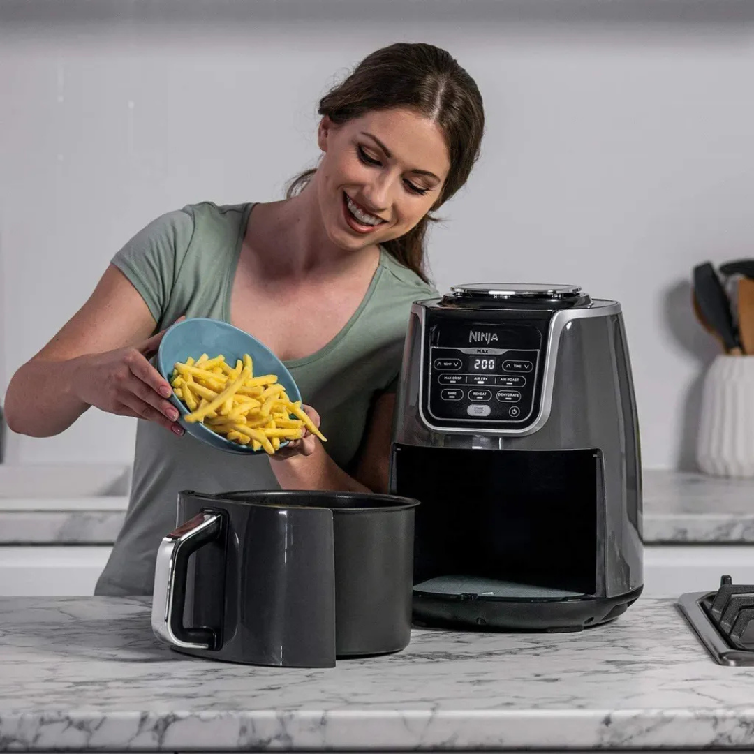 Eine Frau gibt Pommes Frites aus einer Schüssel in einen Airfryer.