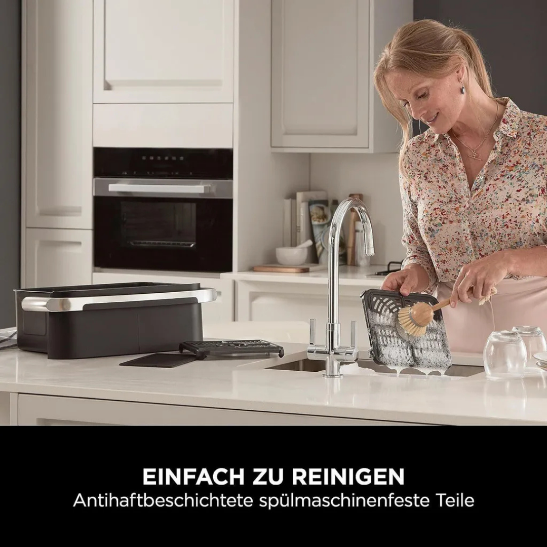 Eine Frau schrubbt einen Grillrost in der Spüle, während ein Gerät daneben steht.