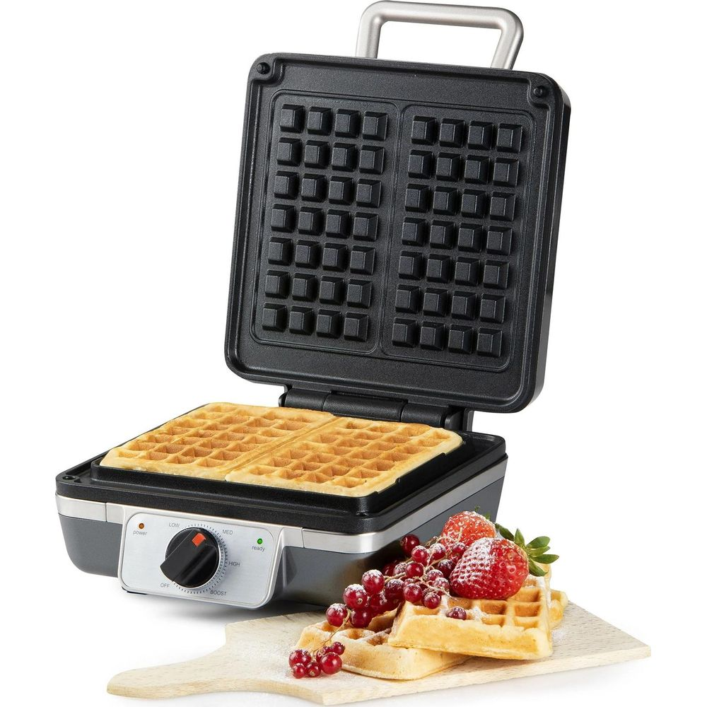 Offener Waffelautomat mit zwei fertigen Waffeln und Beeren auf einem Holzbrett.
