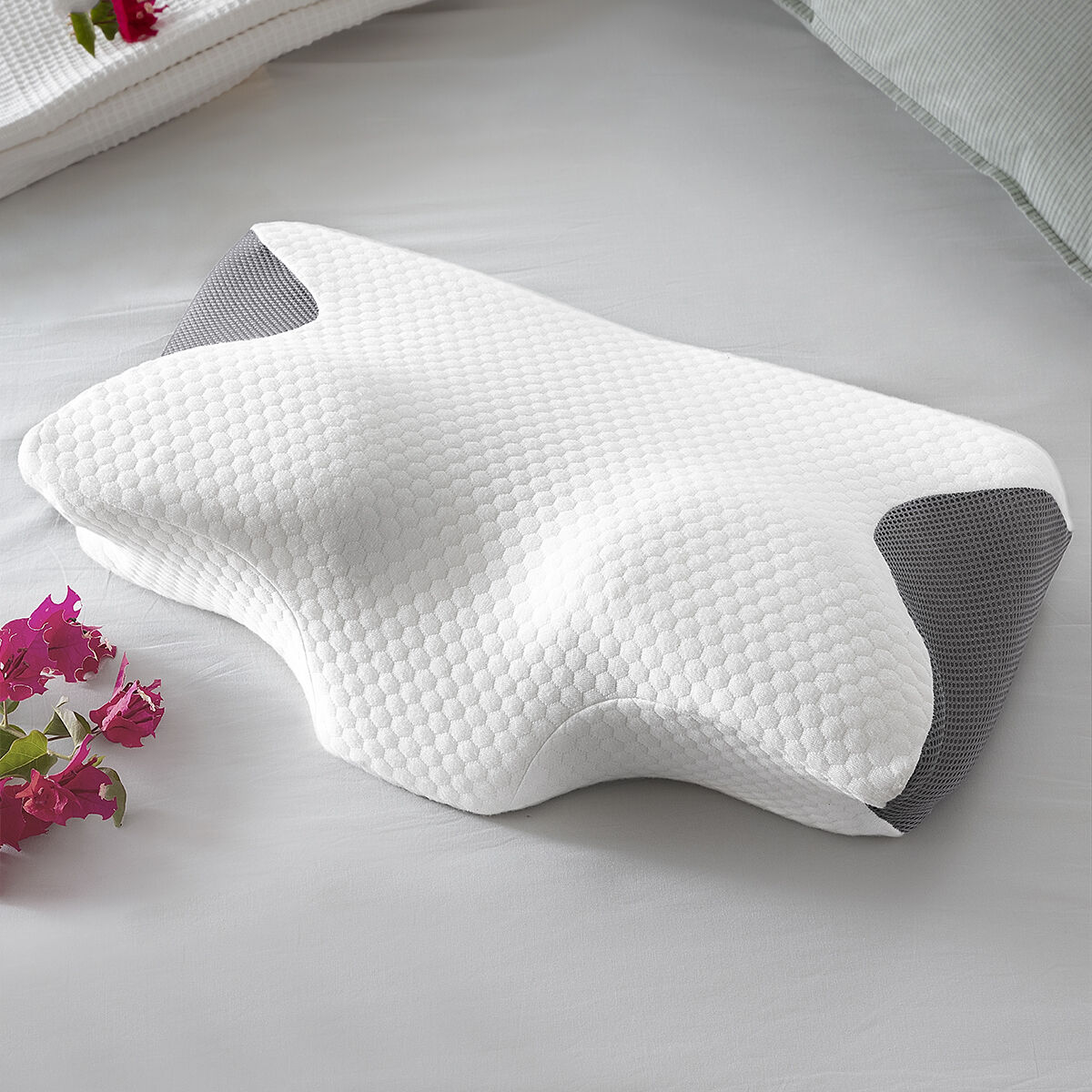 Ein weißes ergonomisches Kissen mit grauen Seiten liegt auf einem Bett.