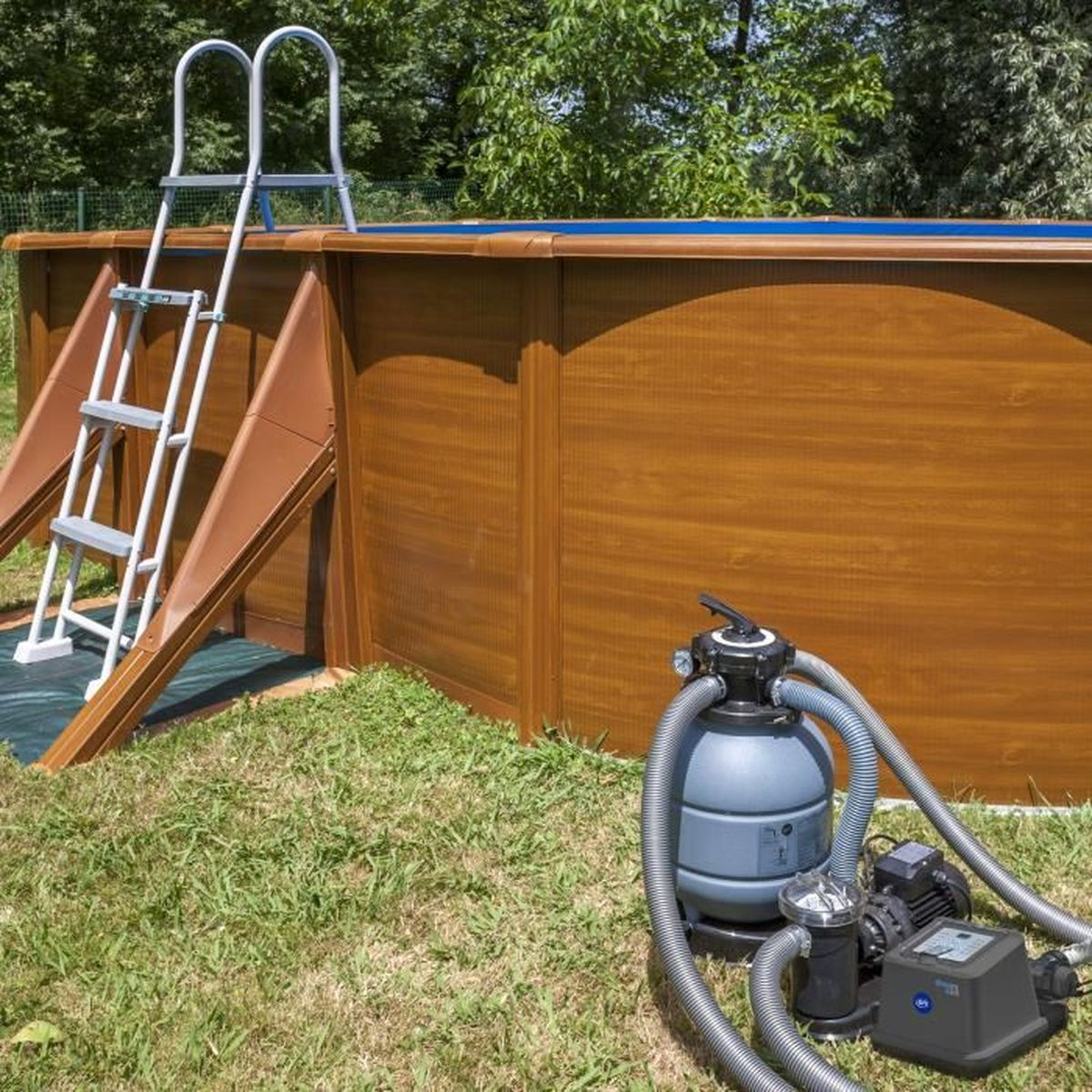 Una piscina de madera con una escalera y un sistema de filtro de arena al lado en el césped.