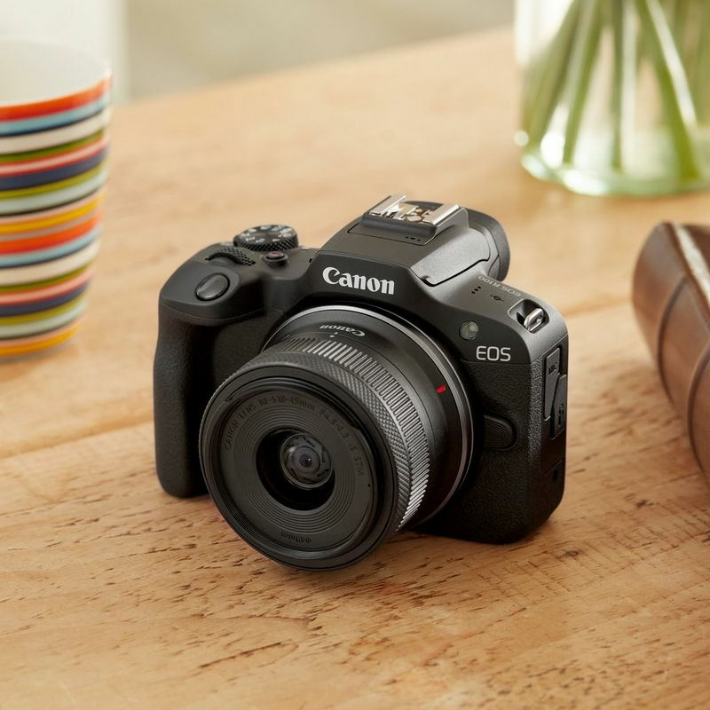 Una cámara Canon EOS negra con lente sobre una mesa de madera.