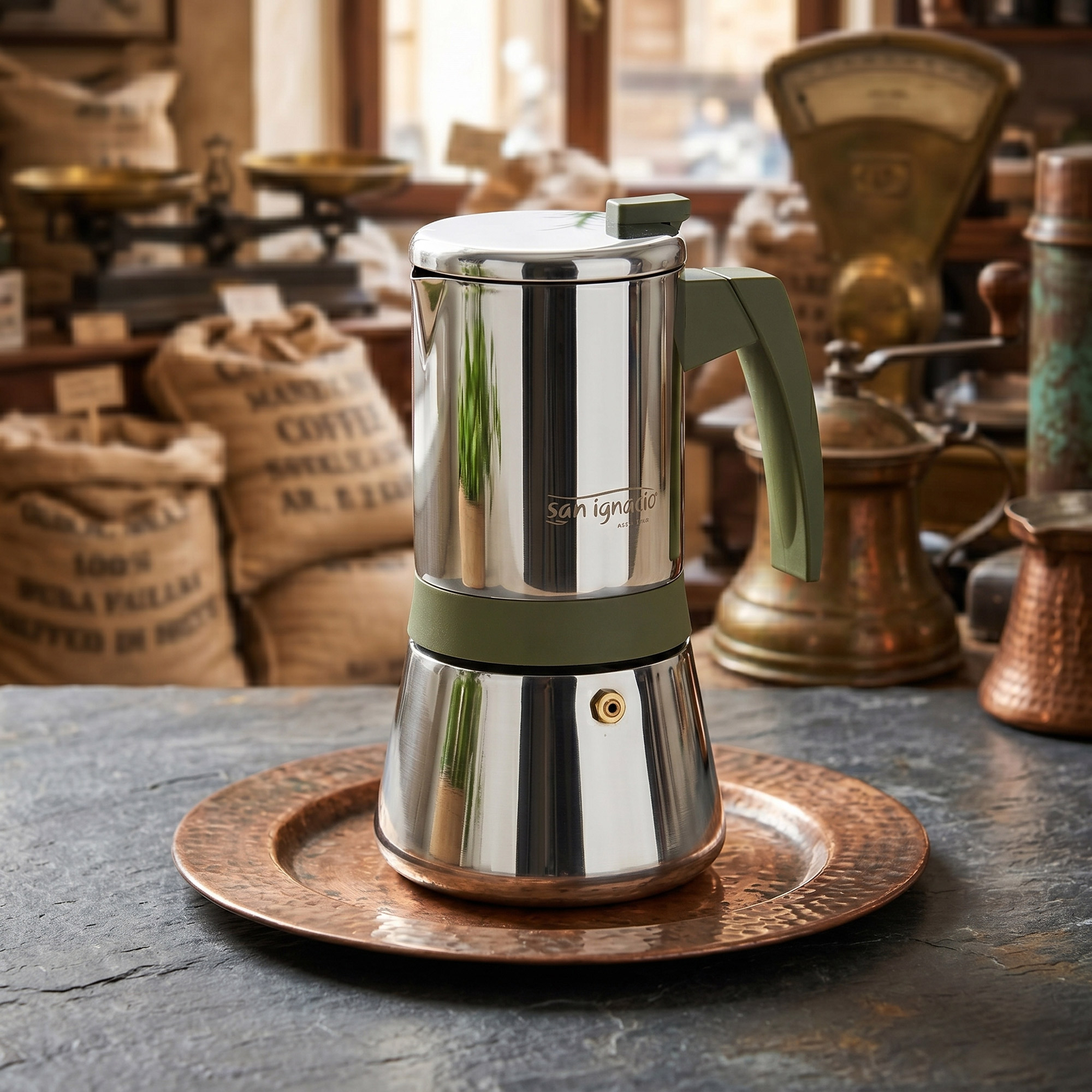 Una cafetera de espresso plateada con asa verde está sobre una bandeja de cobre.