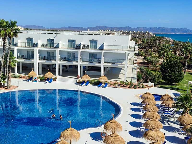 Un hotel moderno con piscina, palmeras y vistas al mar.