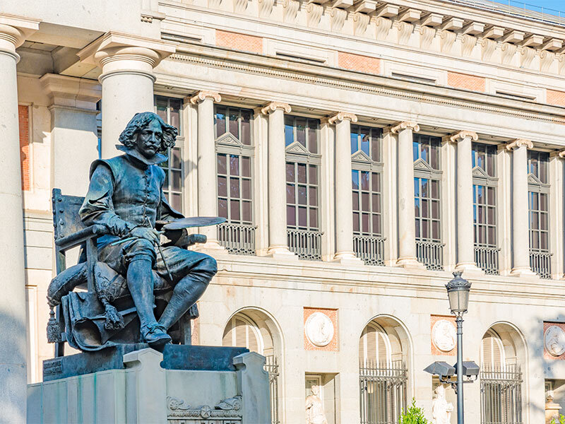 Estatua de bronce de un hombre sentado en una silla frente a un edificio con columnas.