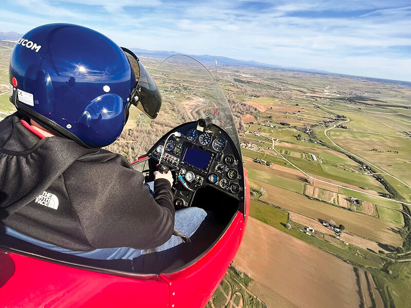 Piloto en un avión rojo vuela sobre un paisaje verde.