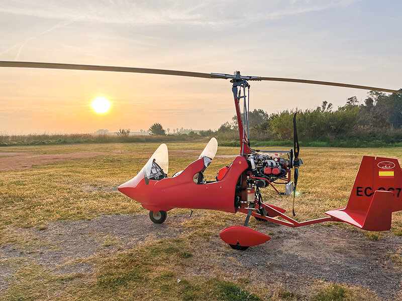 Un autogiro rojo está en un campo al atardecer.