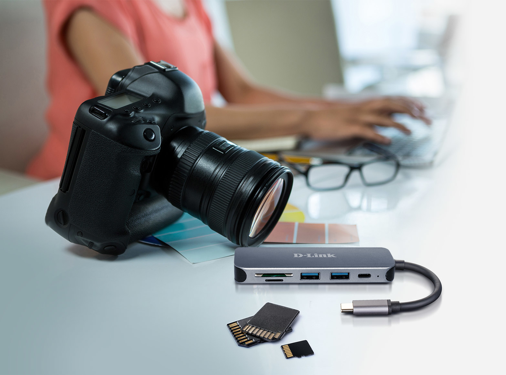 Una fotocamera digitale, schede SD e un hub USB riposano su una scrivania.