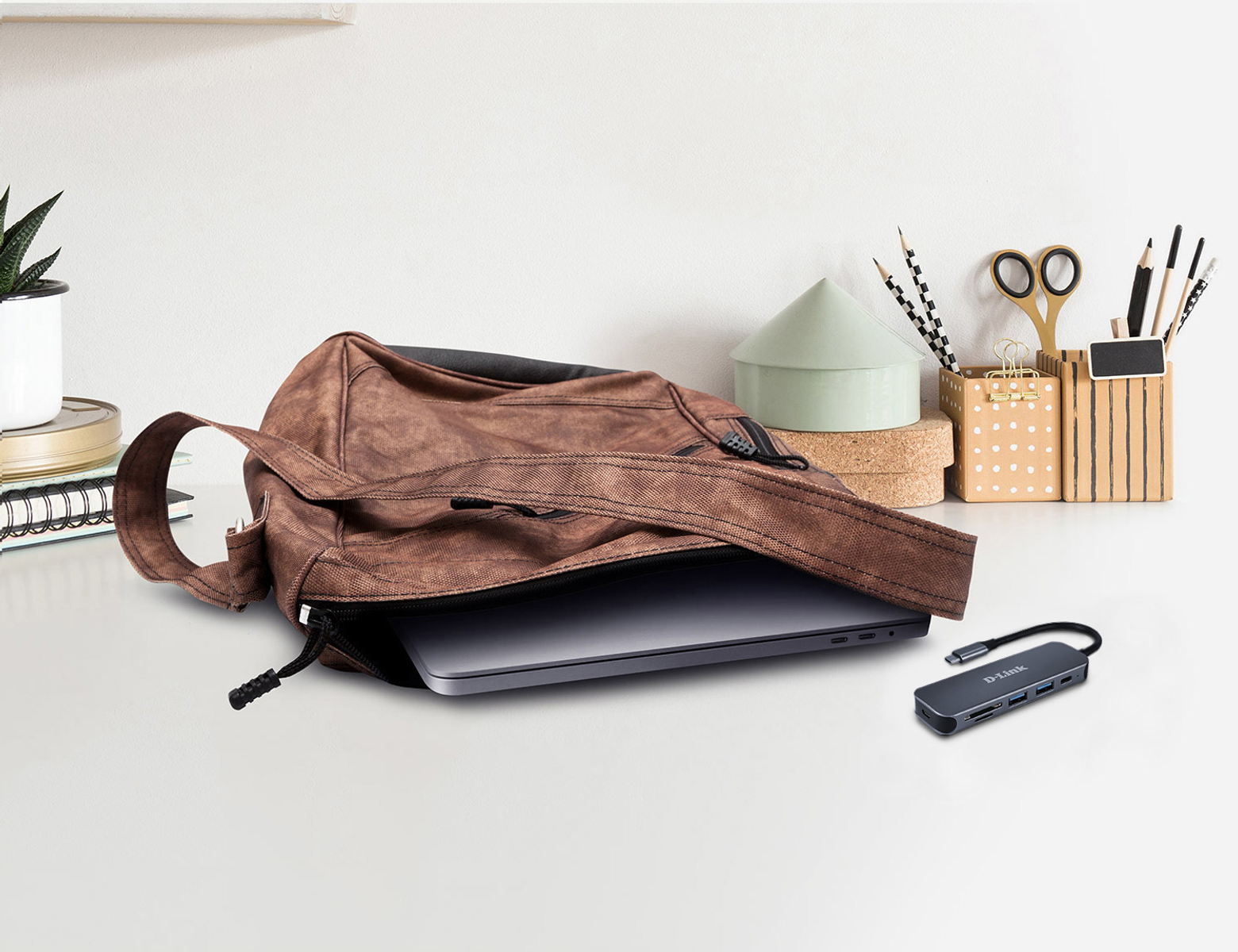 Un laptop è in una borsa marrone su una scrivania, accanto a un hub USB.