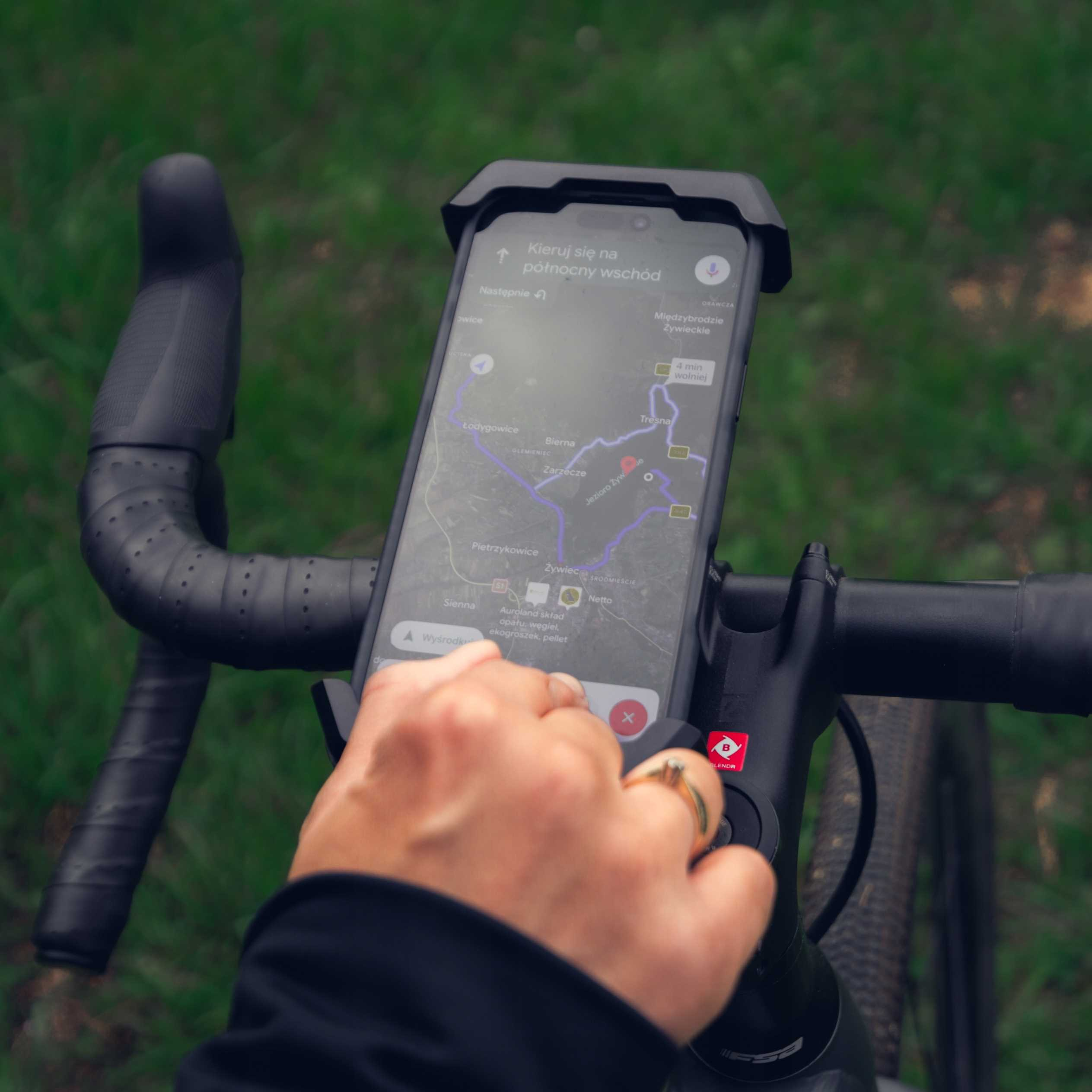 Ręka trzyma smartfon z aplikacją nawigacyjną na kierownicy roweru.