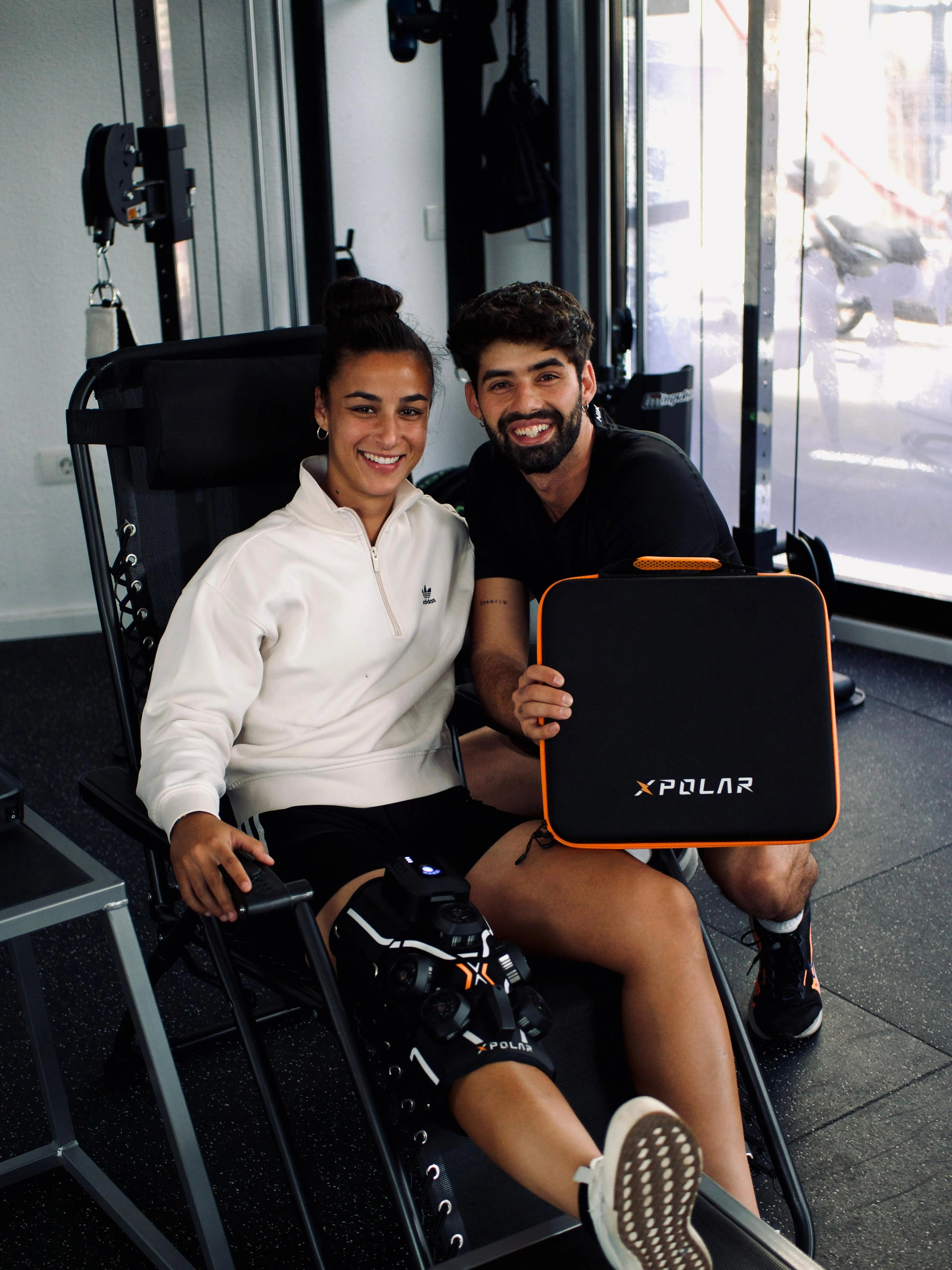 Due persone sorridenti in palestra, una tiene una valigetta nera.
