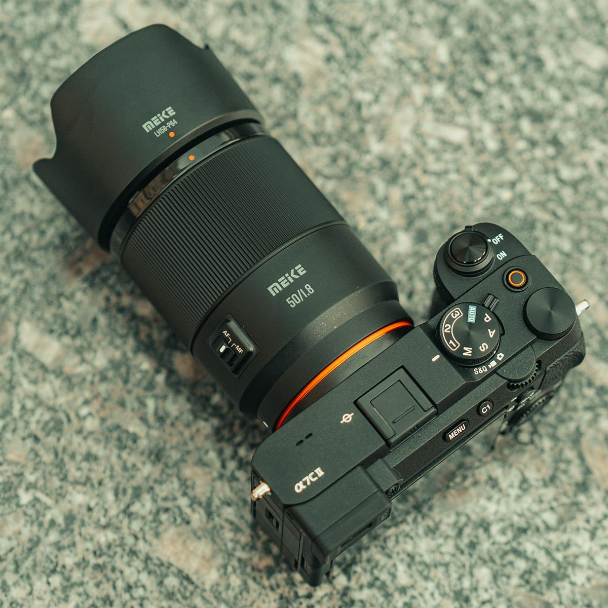 Eine schwarze Kamera mit einem Objektiv mit der Aufschrift 50/1.8 liegt auf einem grauen Steinuntergrund.
