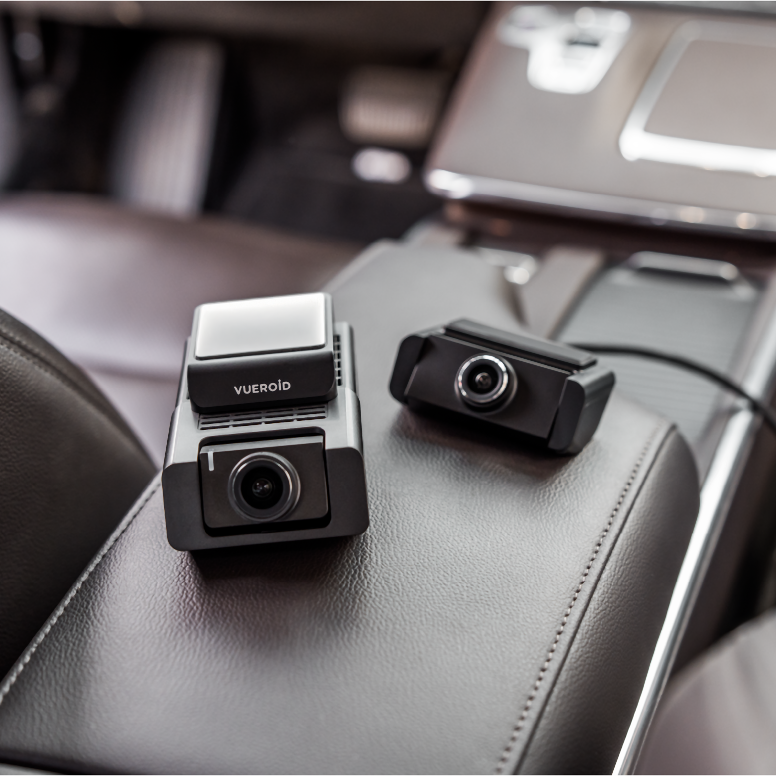 Twee zwarte dashcams op de leren armsteun van een auto. Eén is groter met scherm.