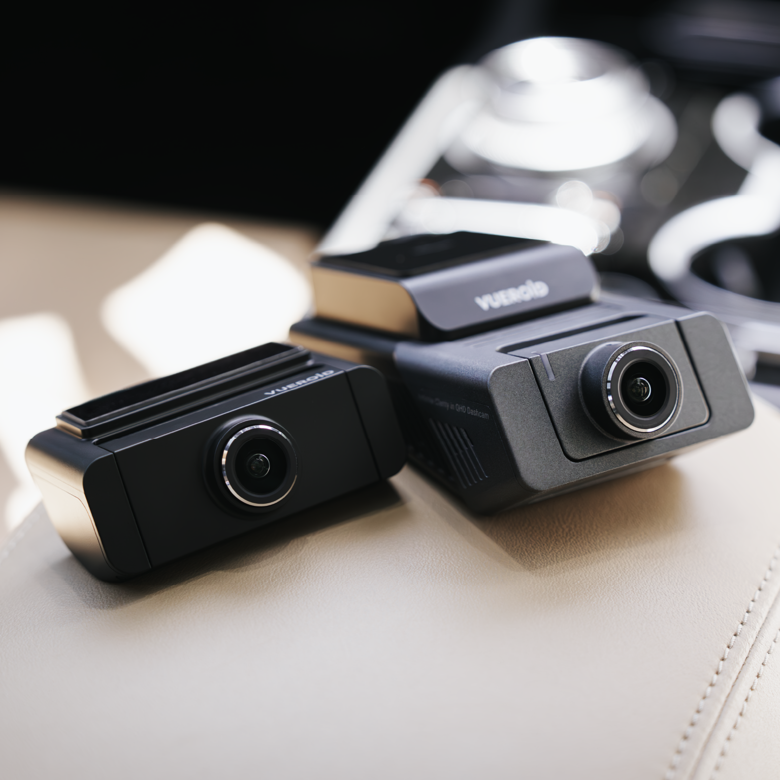 Twee zwarte dashcams rusten op een lichtbeige oppervlak in een auto.