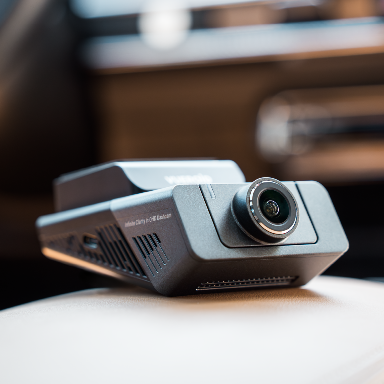 Een zwarte dashcam met lens ligt op een lichtgekleurd oppervlak. Tekst: 'Infinite Clarity in QHD Dashcam'.