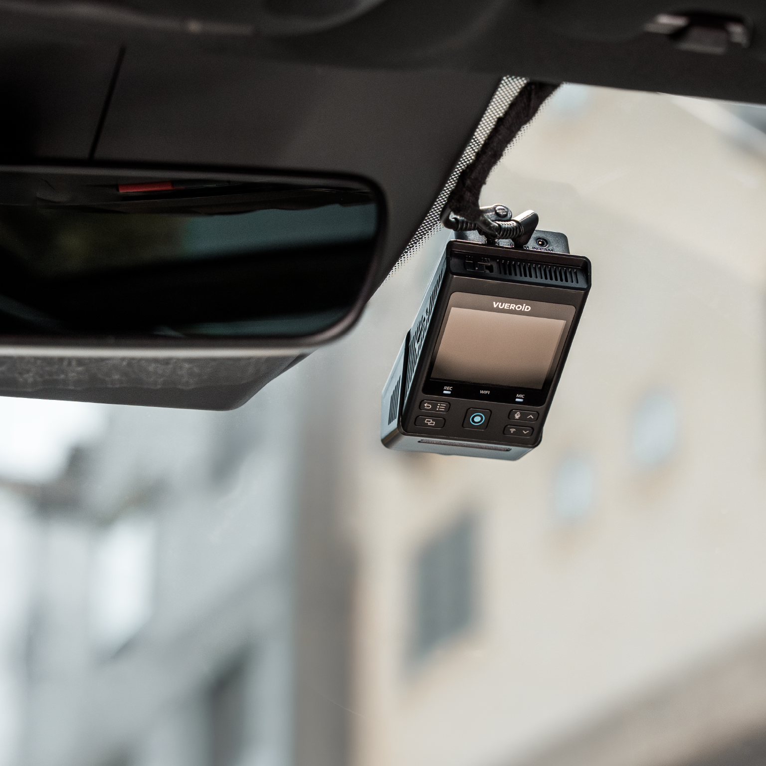 Een zwarte Vueroid dashcam met scherm hangt aan de voorruit.