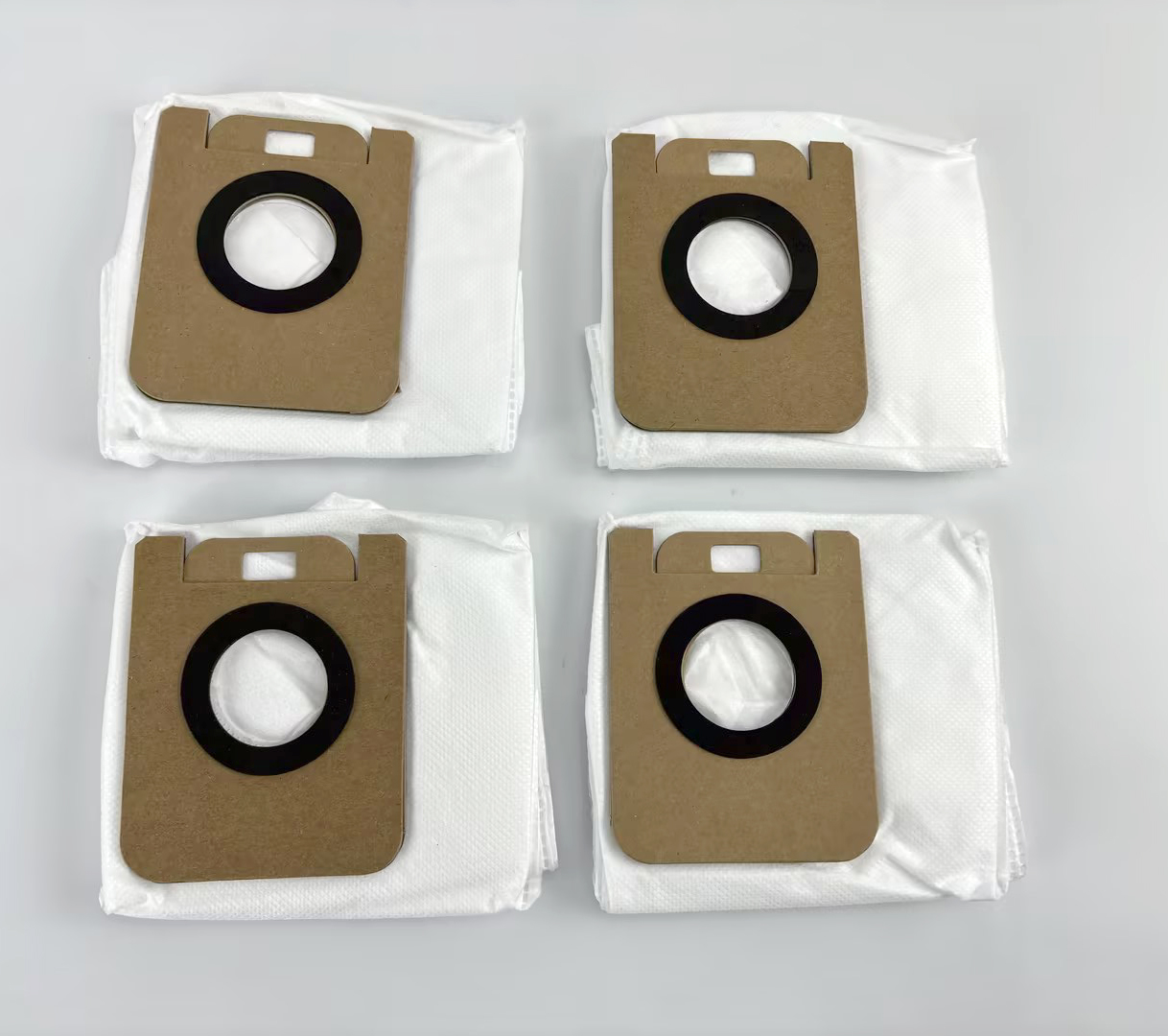 Four white vacuum cleaner bags with brown cardboard tops and black rings.