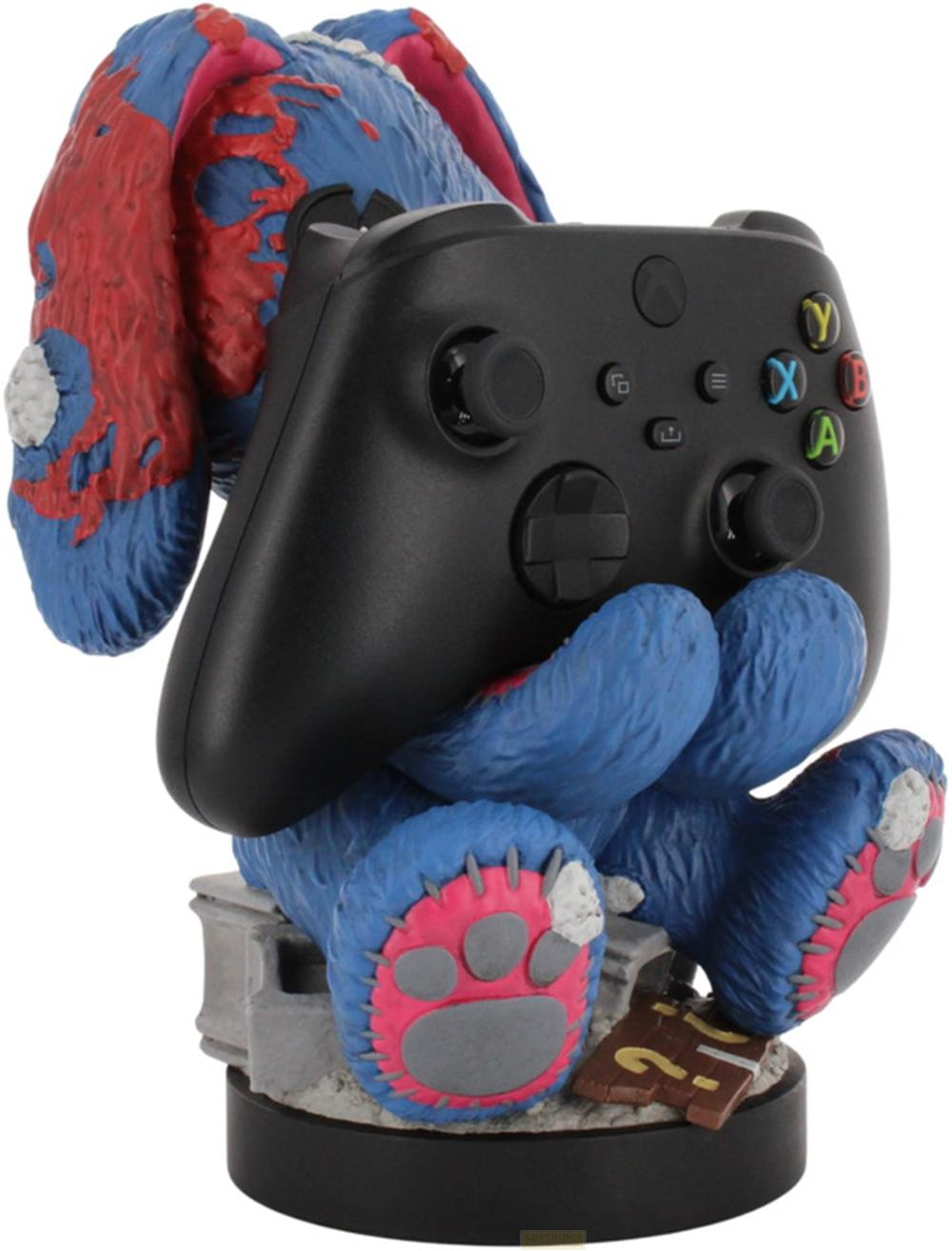 Ein blaues Plüschtier mit roten Flecken hält einen schwarzen Xbox-Controller auf einem Sockel.
