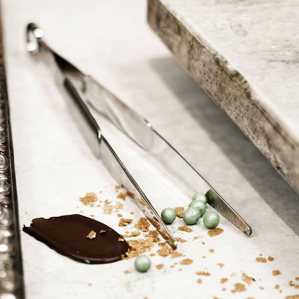 Pinzette tengono sfere verdi vicino a cioccolato e briciole su carta.